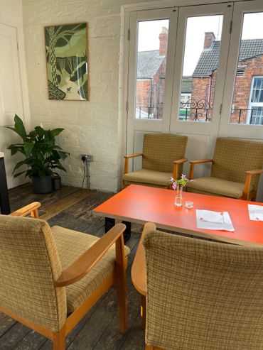 Cozy seating area with vintage chairs and an orange table in a room with rustic wooden floors.