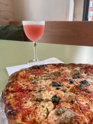 A close-up of a pizza and a pink cocktail on a table.