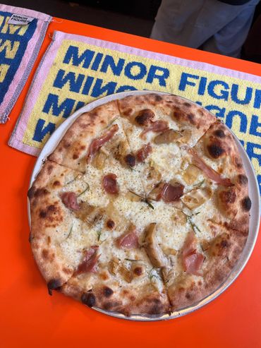 Wood-fired pizza on a bright orange table with a colorful towel.