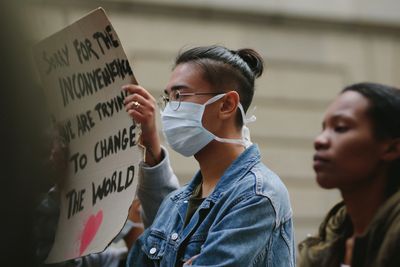 Person wearing mask holds protest sign about changing the world.