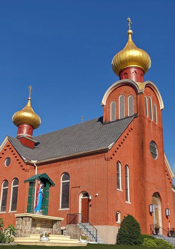 A red brick church with golden onion domes under a clear blue sky.