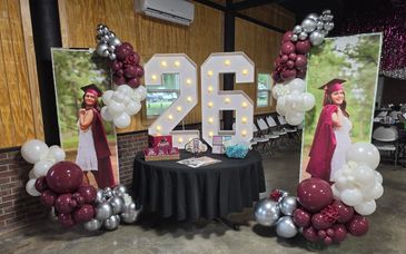 Graduation celebration setup with large illuminated '26' and balloons.