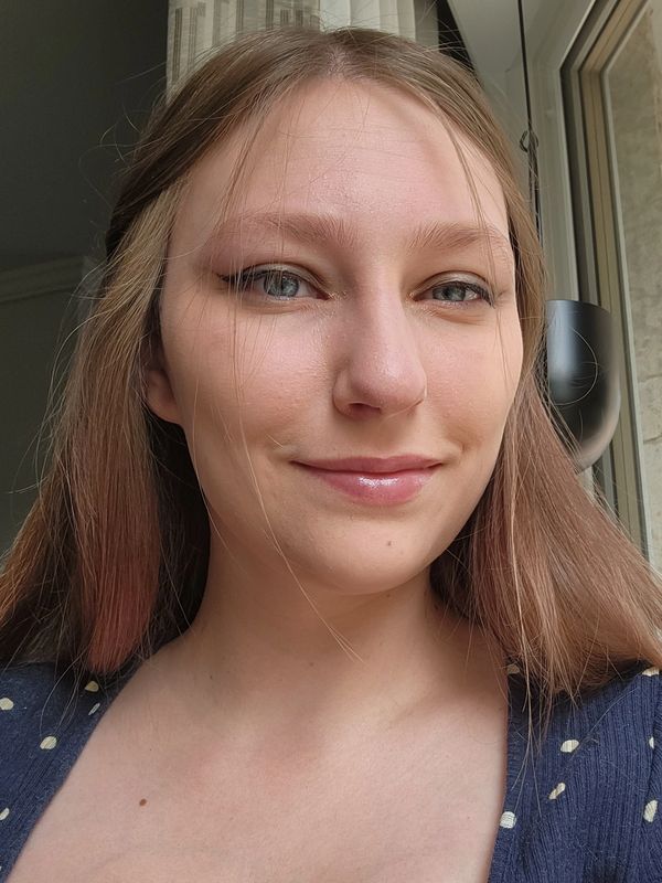 Young woman with long hair smiling near a window.