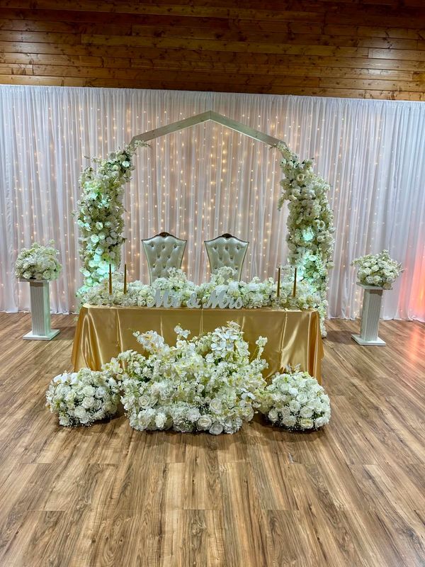 Sweetheart table and wedding arch with wedding floral arrangements and twinkle lights.