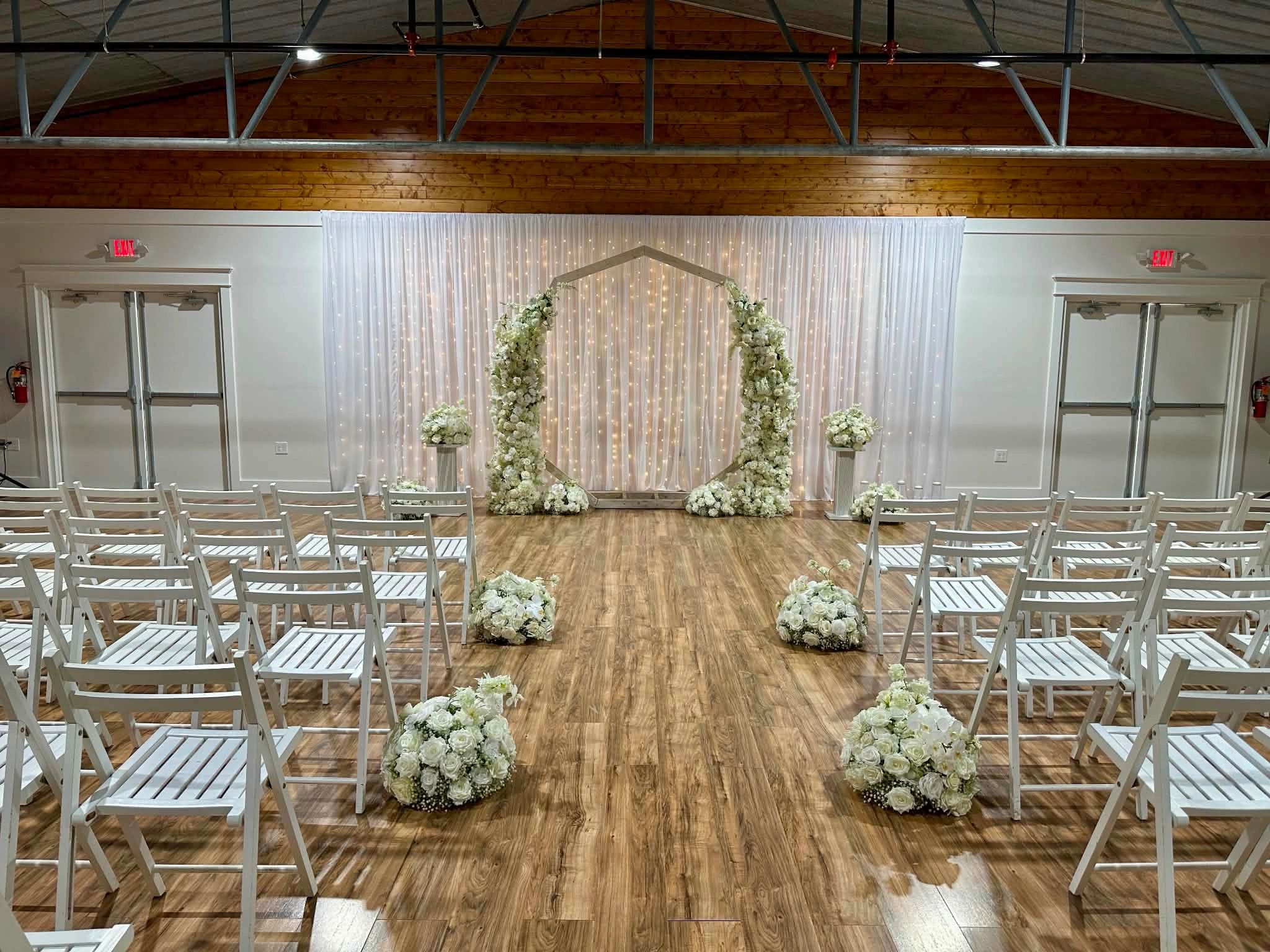 White wedding chairs set up in front of the wedding arch with wedding floral arrangements at The Enc