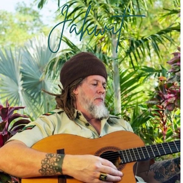 Man with dreadlocks playing guitar in a lush garden.