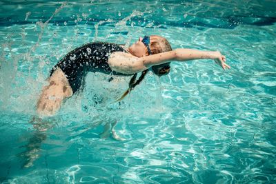 image of girl jumping out of water in a back dive splashing