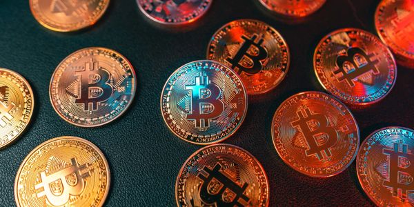 Shiny Bitcoin coins scattered on a dark surface with colorful reflections.