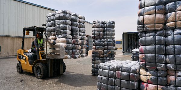 Forklift moving large bundles of wrapped goods outside a warehouse.