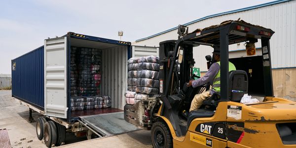 A forklift loads wrapped packages into a shipping container at a warehouse.
