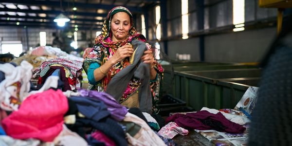 Woman sorting clothes in a warehouse filled with piles of garments.