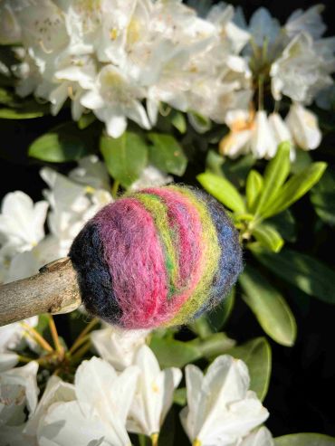 Swirling green, purple and green felted wool on a beater head. Head is on its side.
