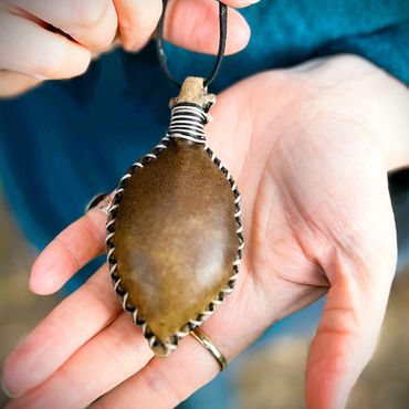 Brown leaf shaped neck rattle with black and white stitching.