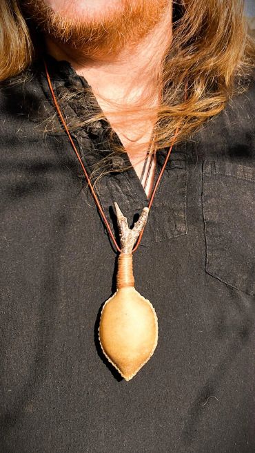 plain leaf shaped neck rattle on leather cord worn by James