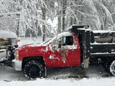 Red truck covered in snow during snowfall.