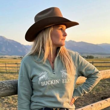Woman in cowboy hat gazing at sunset in a rural setting.
