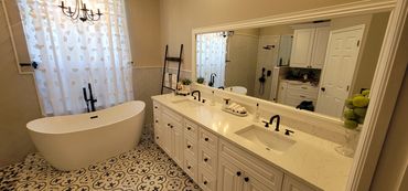 Freestanding tub bathroom with double vanity, quartz countertops, and patterned tile floors