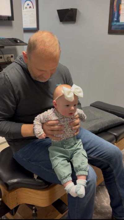 Man holding a baby with a large bow on her head.