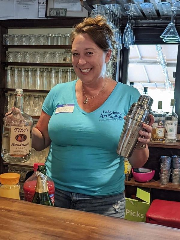 Kristan smiling while making drinks behind a bar, with a bottle of vodka in one hand and a shaker in