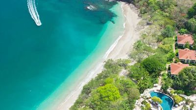 Aerial view of a turquoise beach with a boat and beachfront houses.