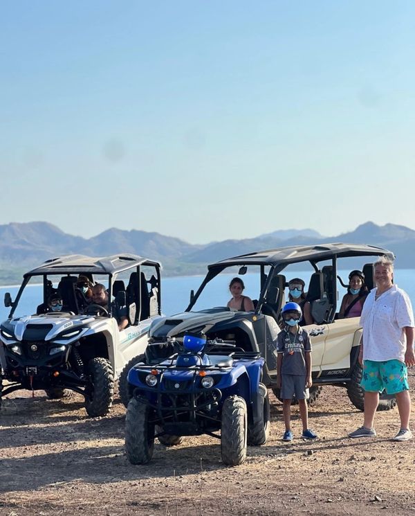 Family with off-road vehicles by the water on a sunny day.