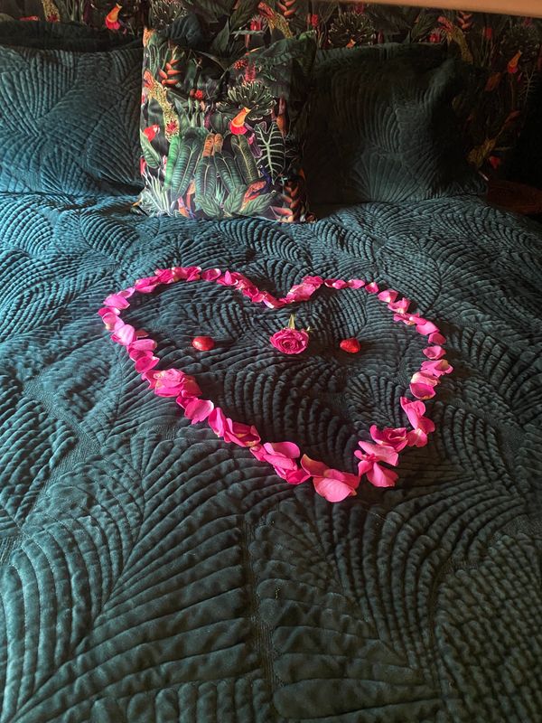 Heart shape made of rose petals on a dark green quilted bedspread.
