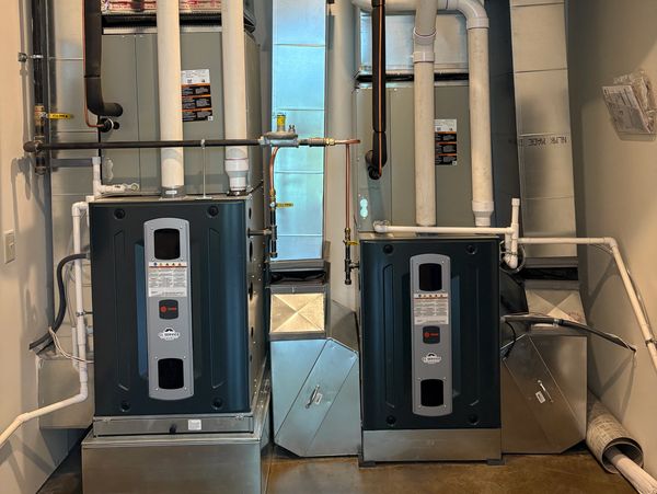Two modern HVAC units with connected ductwork and pipes in a clean utility room.