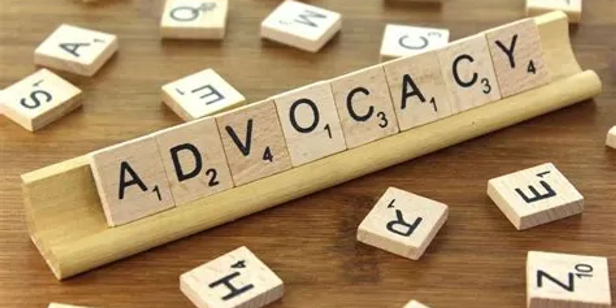Scrabble letters on letter holder spelling ADVOCACY with other letters scattered around.