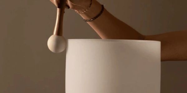 Person holding a white singing bowl with a mallet.
