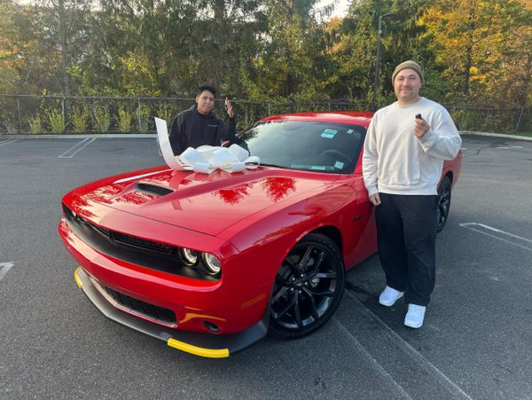 Two men celebrate with a red car adorned with a large white bow and keys in hand.