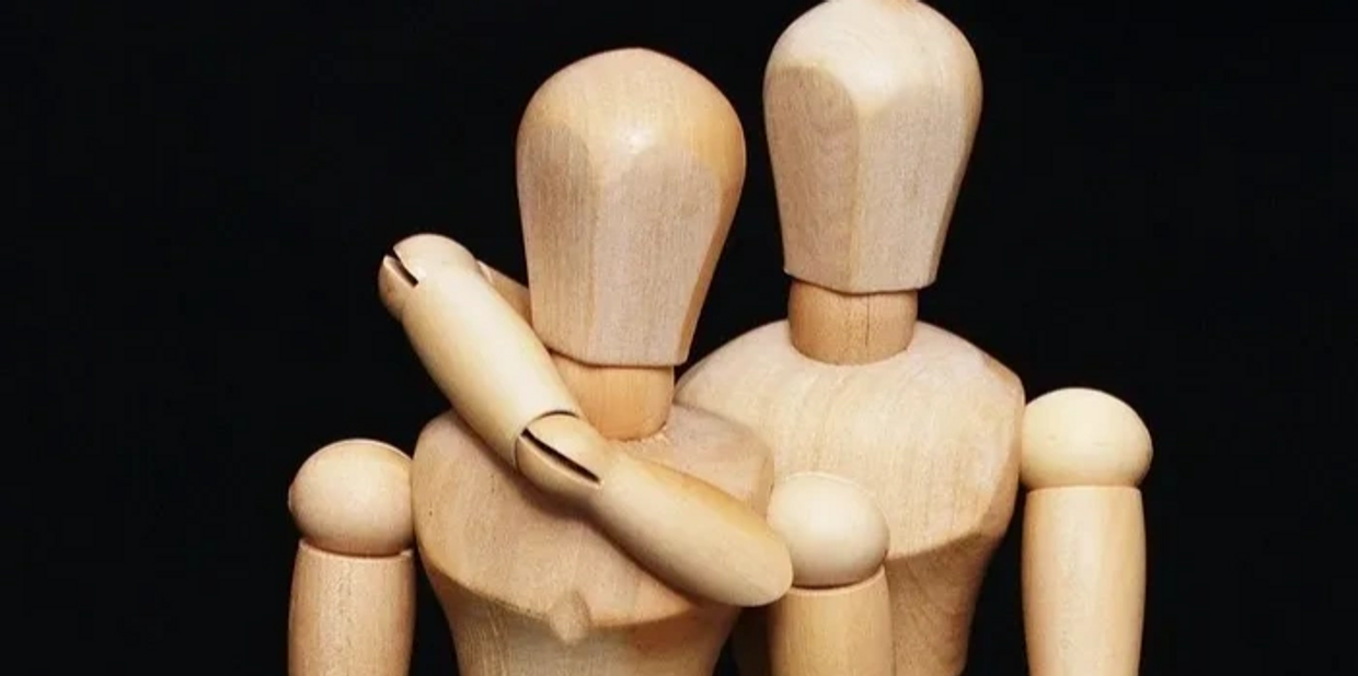 Two wooden mannequins embracing each other against a black background.