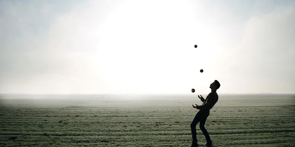 Silhouette of a person juggling three balls in a misty open field.