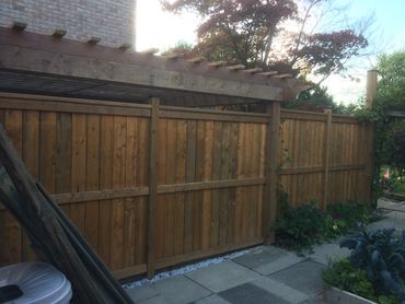 Wooden fence with garden plants and a pergola in backyard.
