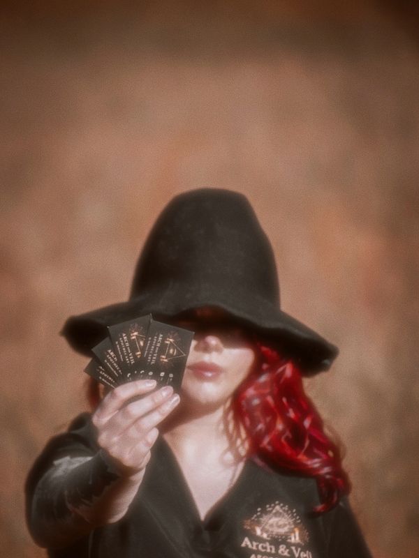 Person with red hair and black hat holding tarot cards.