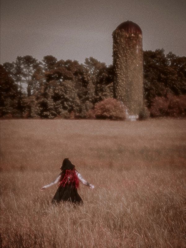 Woman with red hair walks through a field toward an ivy-covered silo.