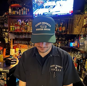 Bartender wearing Casey Moore's Oyster House cap and shirt behind a bar.