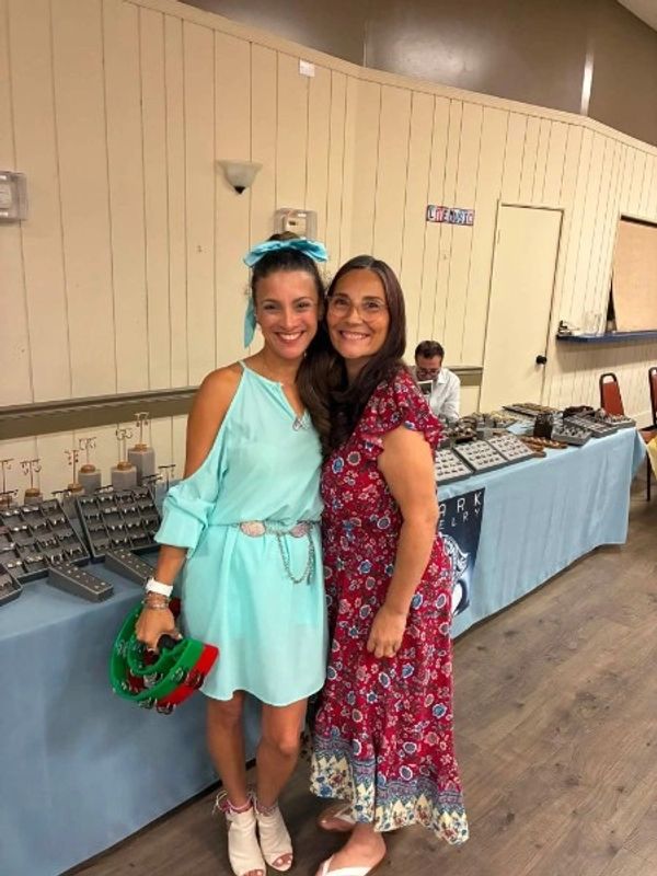 Two women smiling, standing close together at a jewelry display.