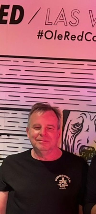 Man smiling in front of a pink wall with text.