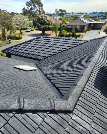 Newly installed dark tile roofs of suburban houses under clear skies.