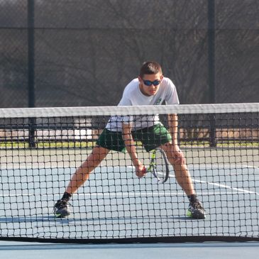 Man in sunglasses playing tennis on an outdoor court.
