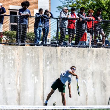 Tennis player serving while spectators watch from above.