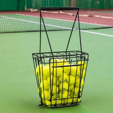 Basket filled with yellow tennis balls on a tennis court.