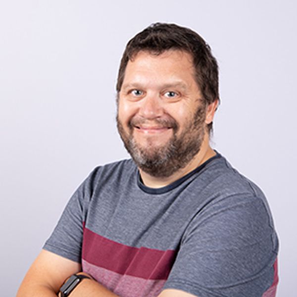 Smiling man with beard in casual t-shirt posing with arms crossed.