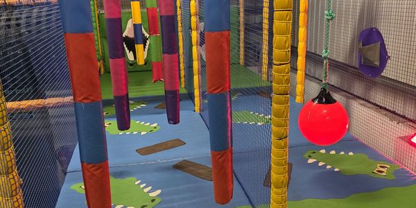 Colorful indoor soft play area with hanging padded obstacles and cartoon crocodile mats.