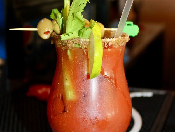 A Bloody Mary cocktail garnished with celery, olives, and a lime wedge.