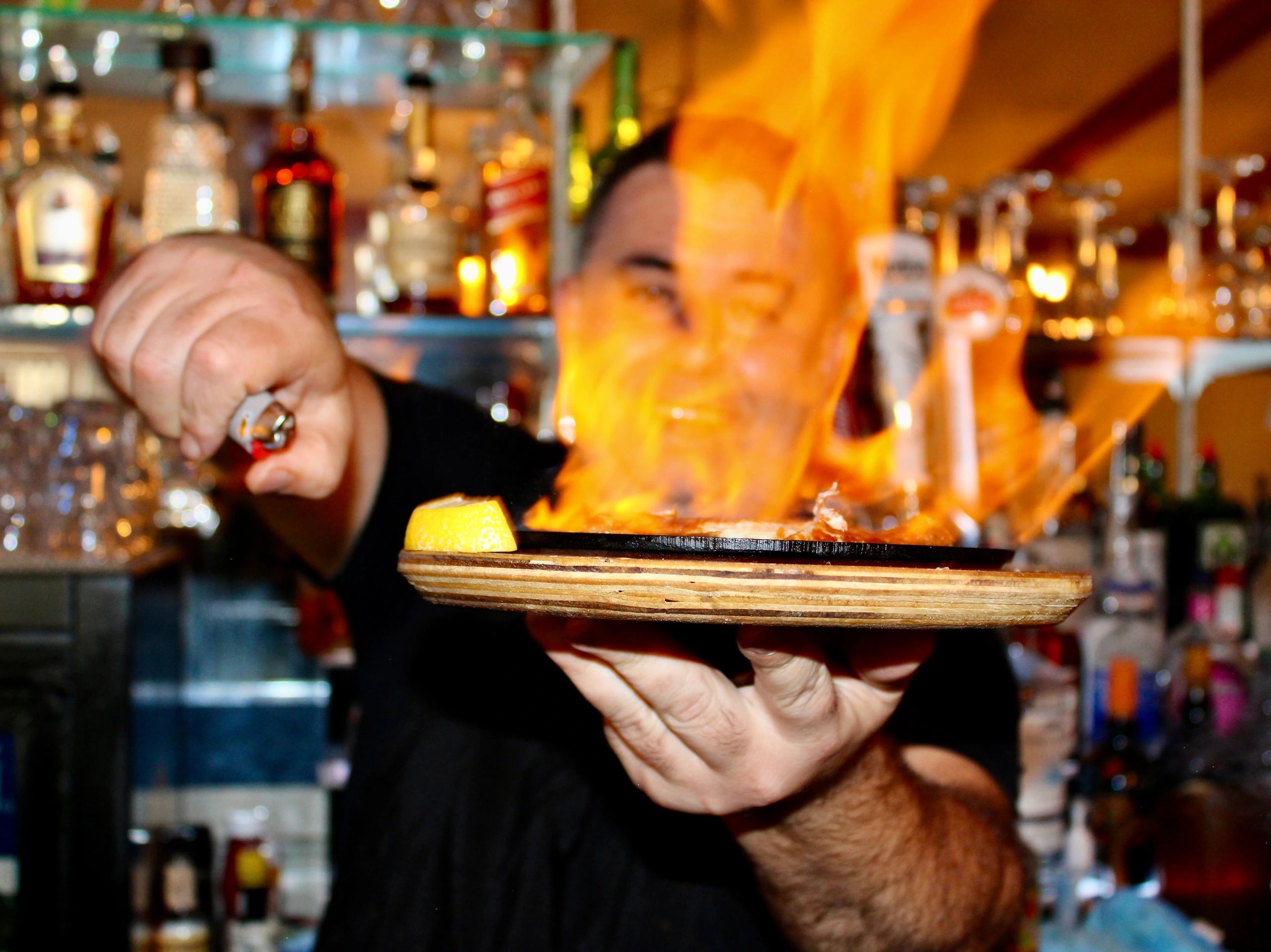 Bartender flambéing Saganaki with a lighter behind a bar.