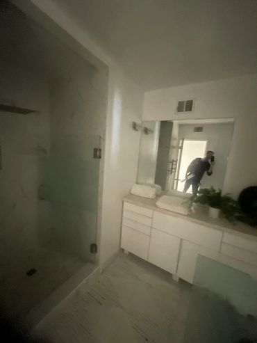 A person cleaning a modern white bathroom with glass shower doors.