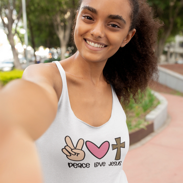 Smiling young woman taking a selfie, wearing a tank top with peace, love, and Jesus symbols.