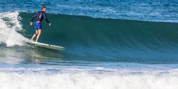 Surfer rides a clean wave in the ocean under clear skies.