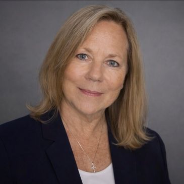 Woman in a dark blue suit and black tie smiling gently.